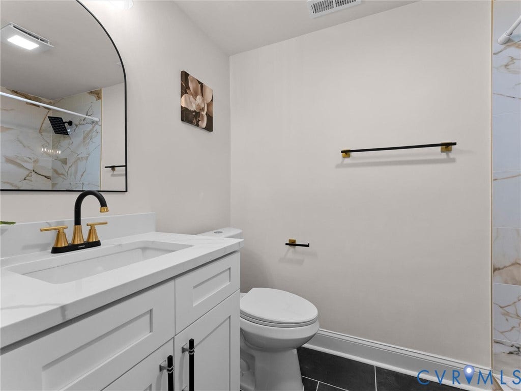 White vanity with a solid surface countertop, black and gold-tone faucet, arched mirror, and dark tile flooring