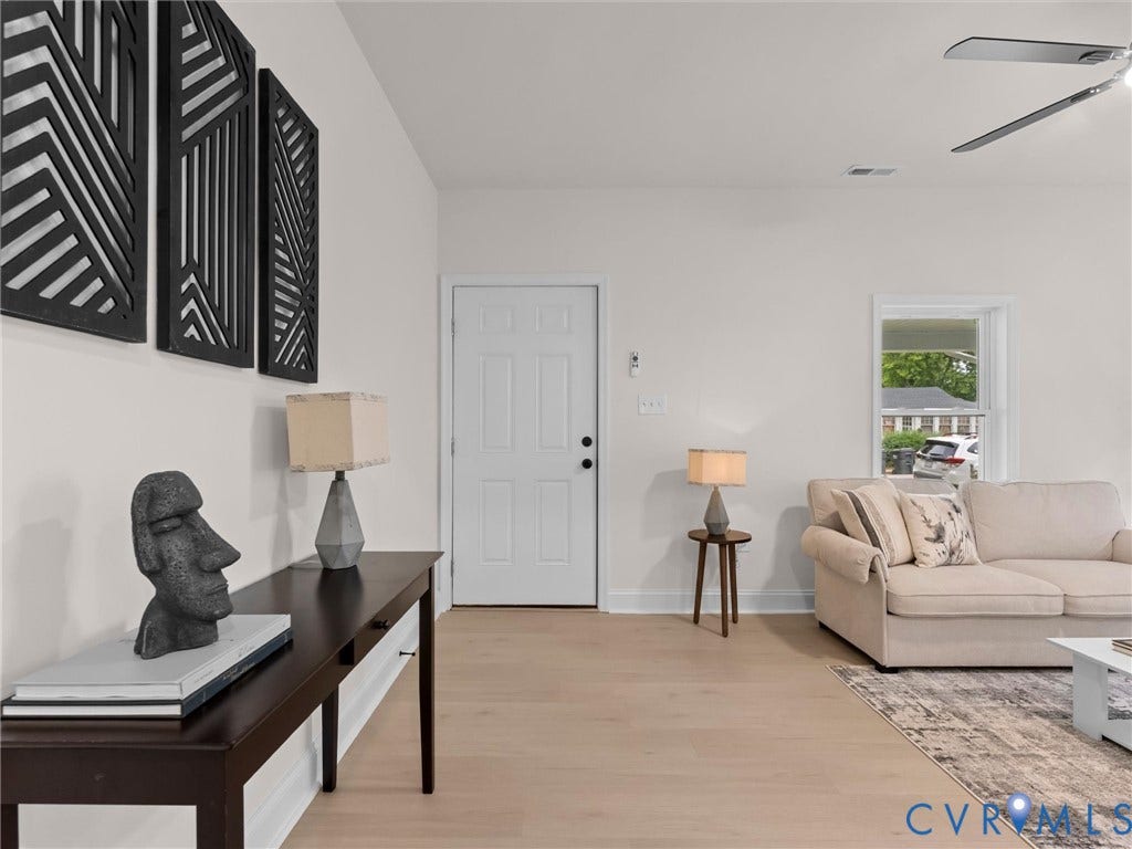 Light wood-finish flooring, white walls, white paneled door, and a ceiling fan with integrated lighting