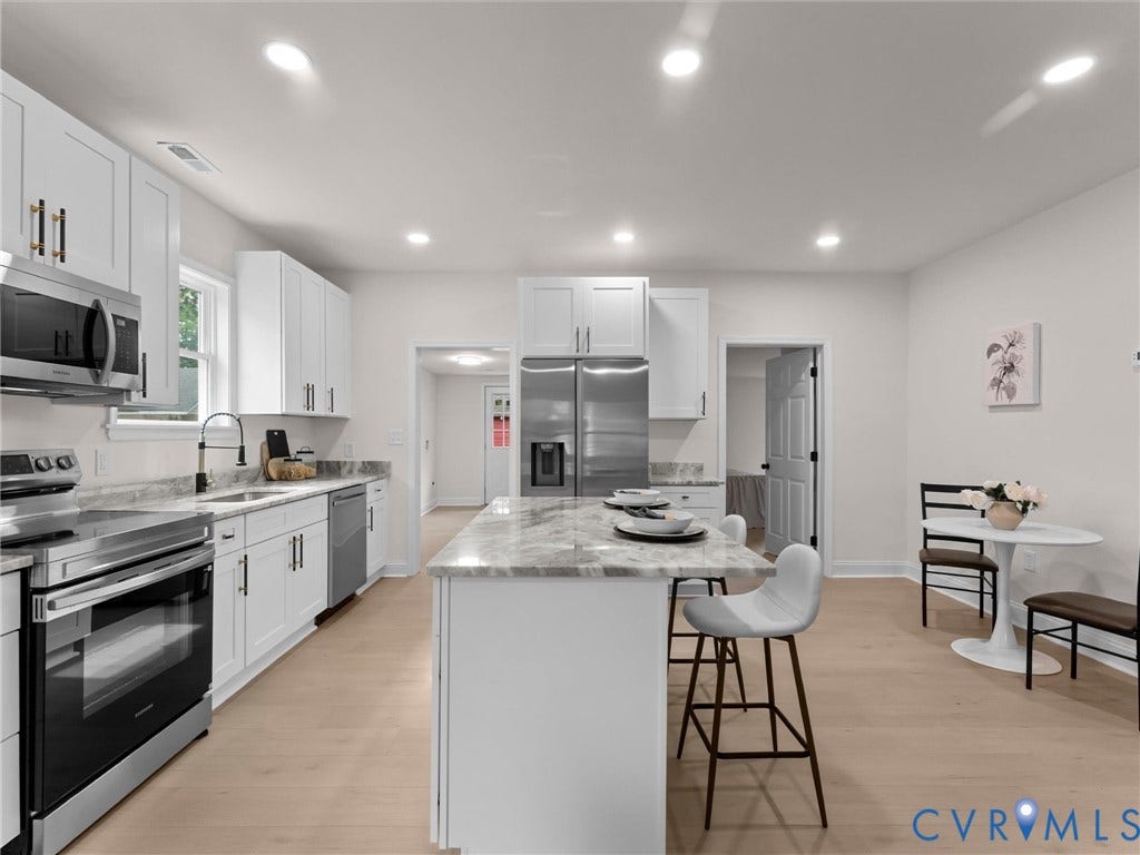 White shaker-style cabinetry with matte black hardware, stainless steel appliances, light-toned wood-finish flooring, recessed lighting, and a kitchen island with a stone countertop