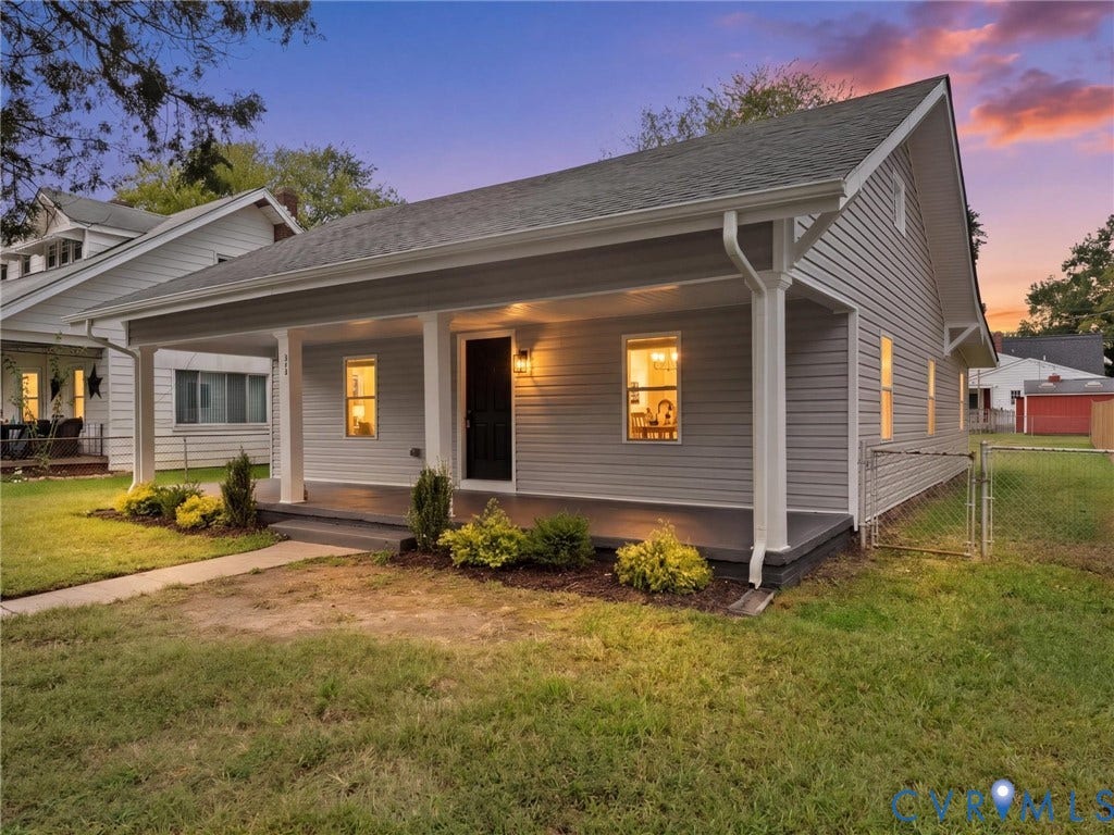 Covered front porch, gray horizontal siding, dark roof, front yard with green grass, and low-maintenance landscaping