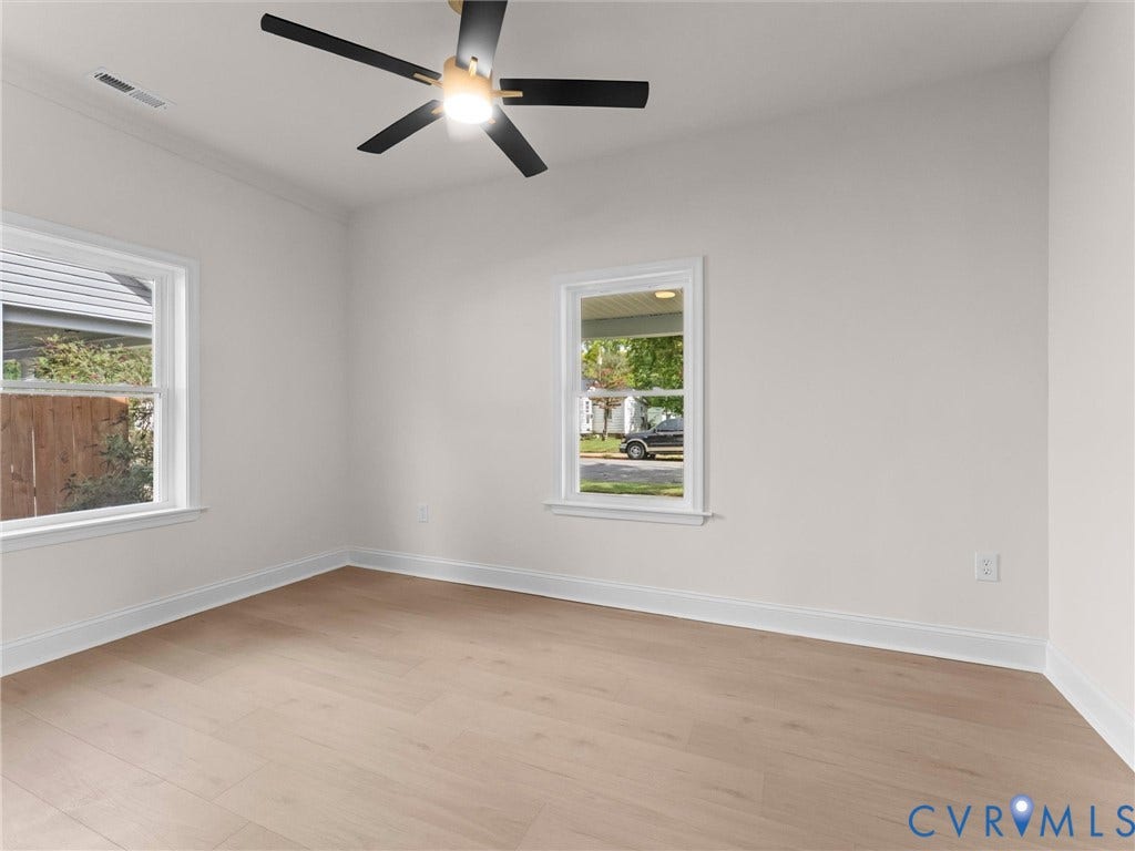 Wood-finish flooring with crisp white trim, two windows, and a ceiling fan with light fixture