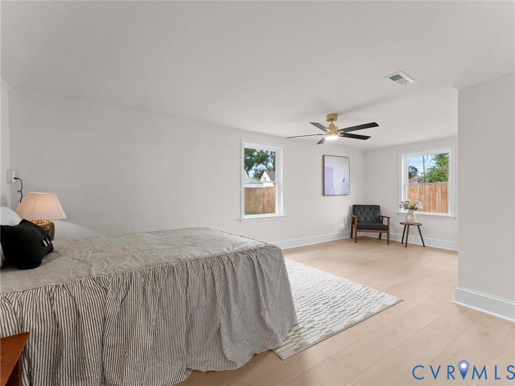 Light wood-finish flooring, two large windows, a ceiling fan with integrated lighting, and crisp white walls