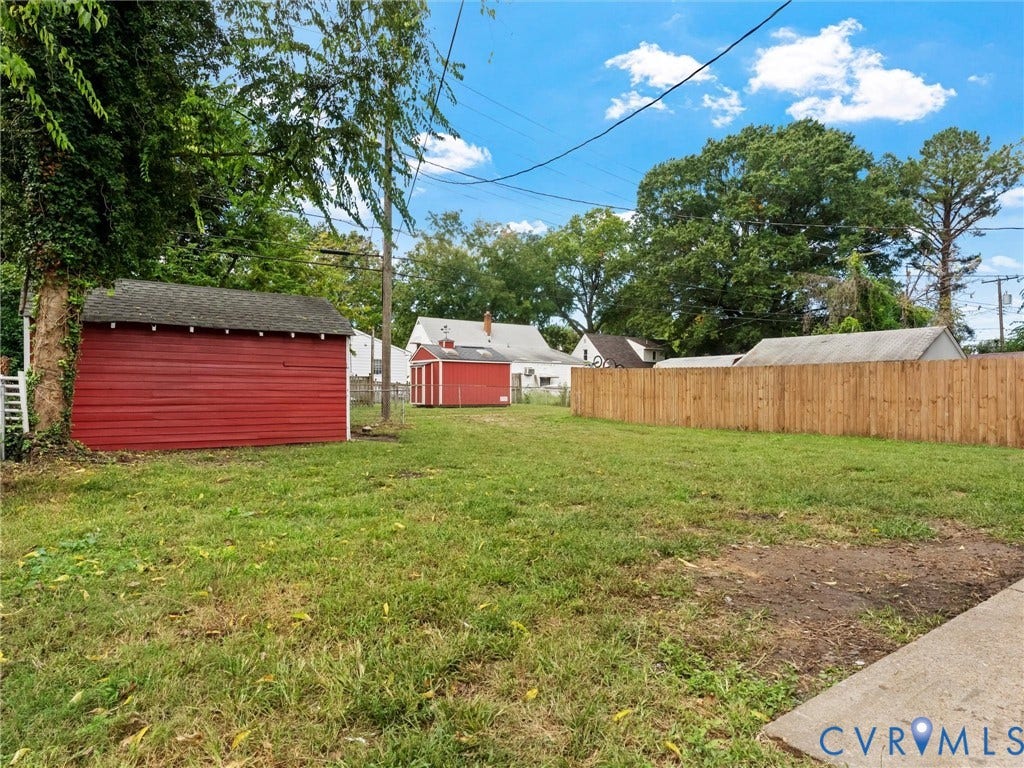 Expansive yard featuring a wooden privacy fence, two red storage sheds, and mature trees