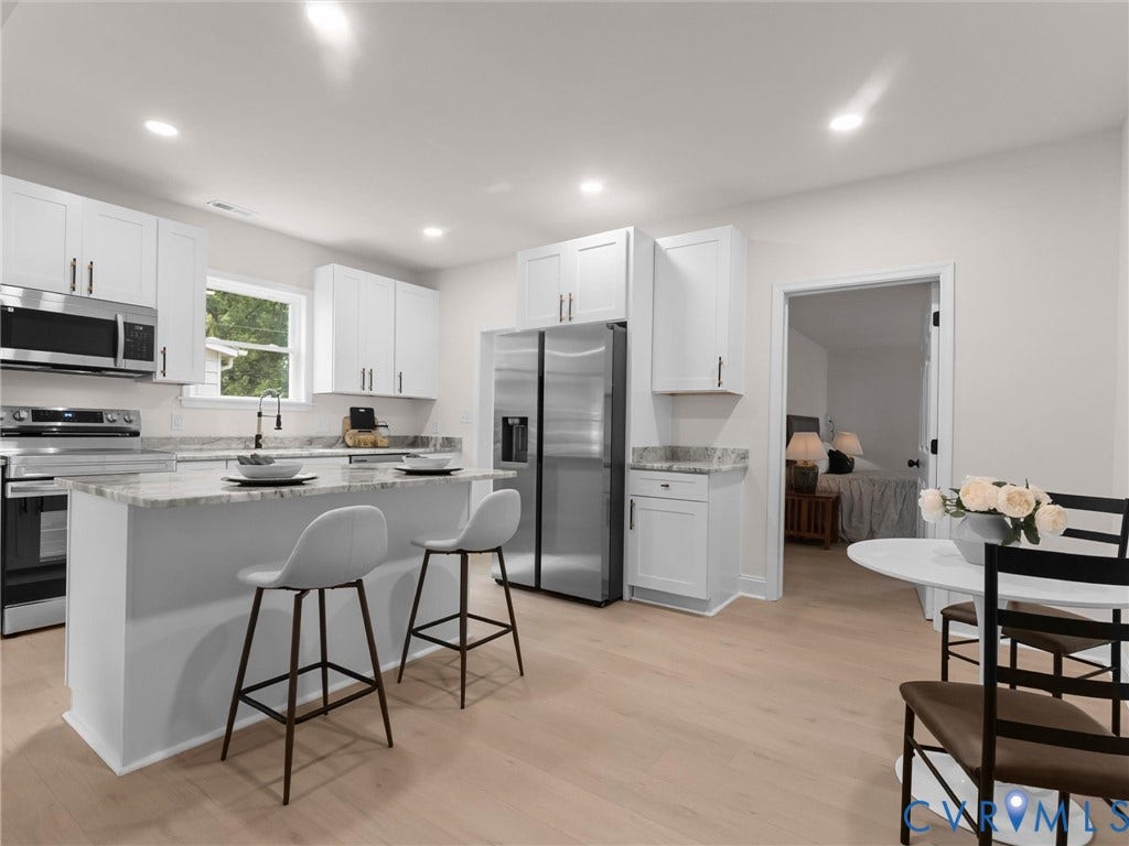 Kitchen featuring white cabinetry, stainless steel appliances, a center island with counter seating, and wood-finish flooring
