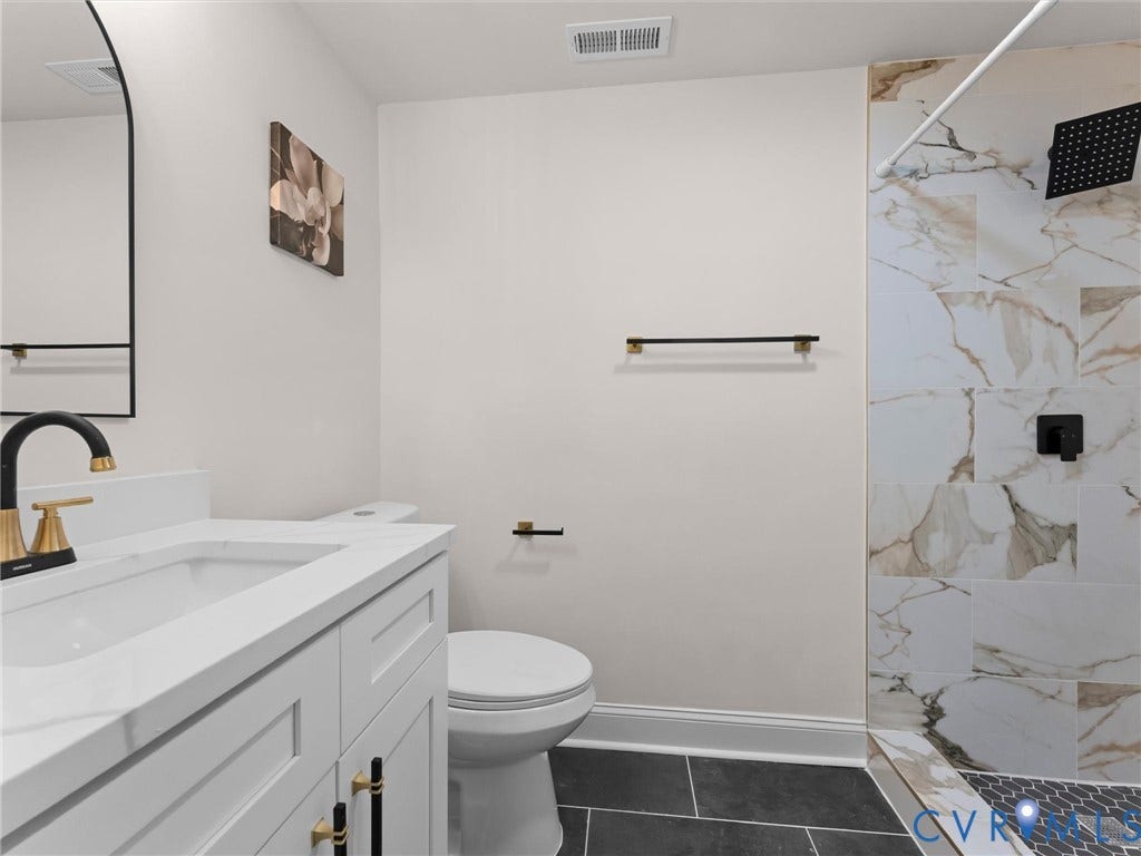 White vanity with gold-accented hardware, black and gold-finish faucet, white countertop, and dark gray tile flooring