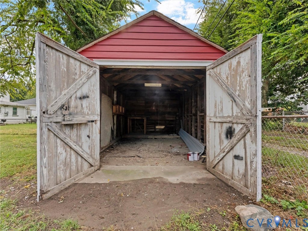 Detached garage structure with red siding, double wooden barn doors, and a concrete threshold