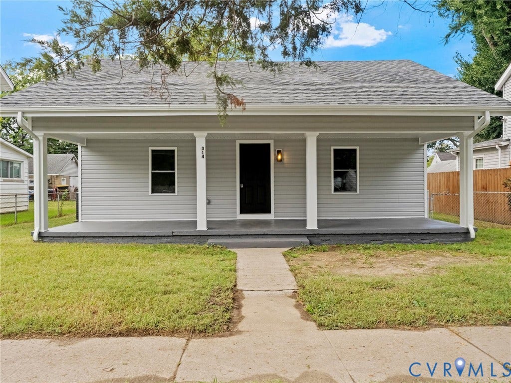 Exterior featuring a covered front porch, white columns, gray siding, a dark entry door, and a gray shingle roof