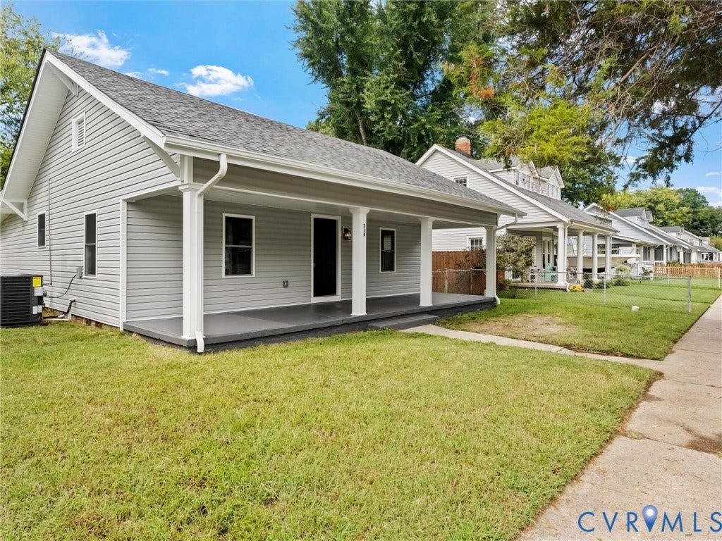 Gable roofline, light gray siding, covered front porch with white columns, concrete sidewalk, and green lawn