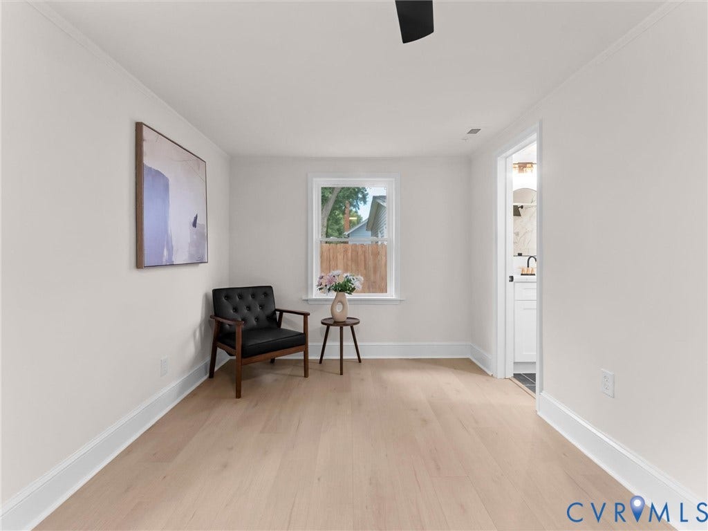 Light wood-finish flooring, white wall paint, crown molding, and a visible doorway to an adjacent room