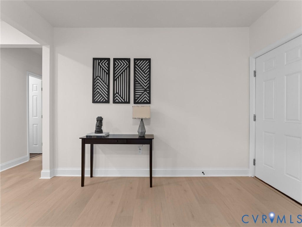 Light-toned wood-finish flooring extending into a separate space, white painted walls, and a white paneled door