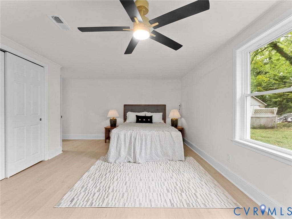 Light wood-finish flooring, a white window frame, and a ceiling fan with black blades and a gold-tone fixture