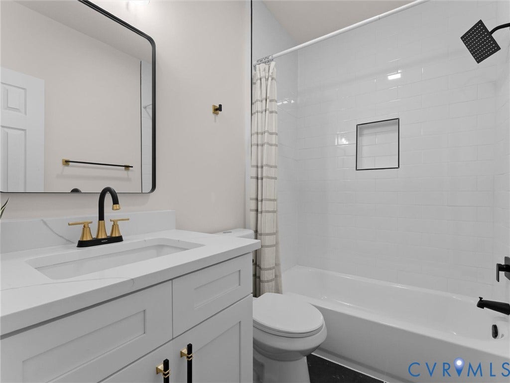 White subway tile shower surround with a built-in niche, modern vanity with integrated sink, gold and black fixtures, and a sleek framed mirror