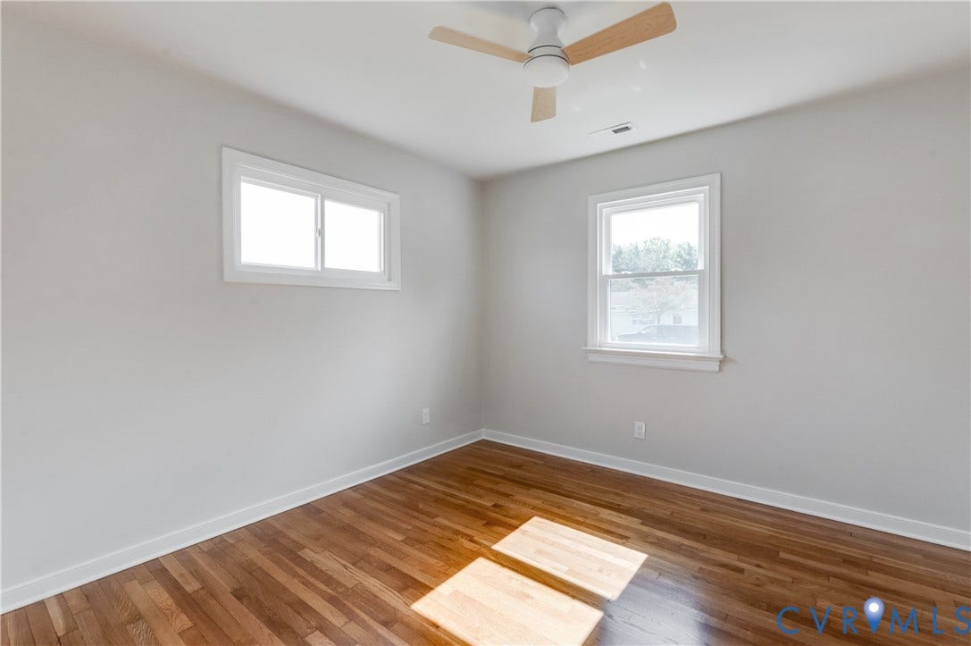 8010 Callison Drive, Glen Allen, VA 23060 Hardwood flooring, white painted walls, two windows with white trim, and a ceiling fan with wood-finish blades