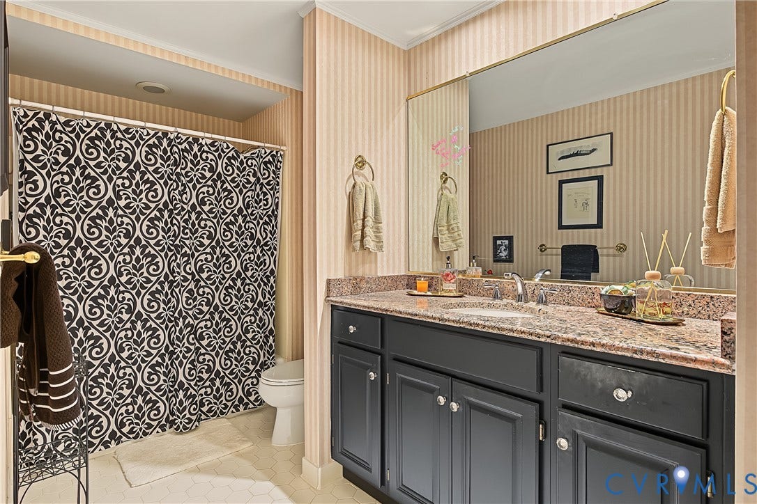 3131 Stony Point Road, #B, Richmond, VA 23235 Bathroom featuring a dual-sink vanity with a speckled countertop, a large wall-mounted mirror, a built-in toilet, and patterned wallpaper