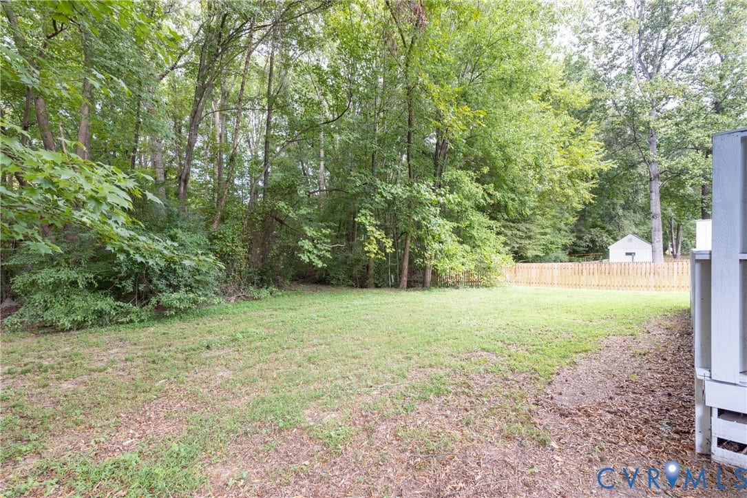 Expansive backyard with a manicured lawn, bordered by a wooden privacy fence, mature trees, and a utility shed