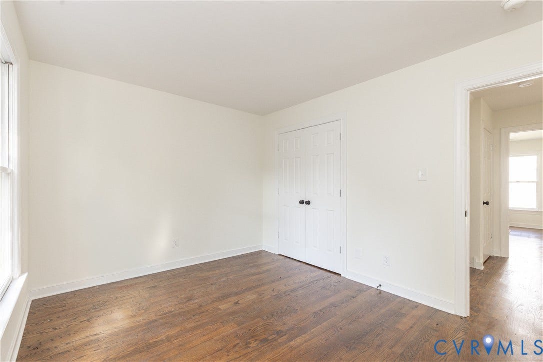 Hardwood flooring, neutral wall paint, white trim, window, and a paneled closet door with dark hardware
