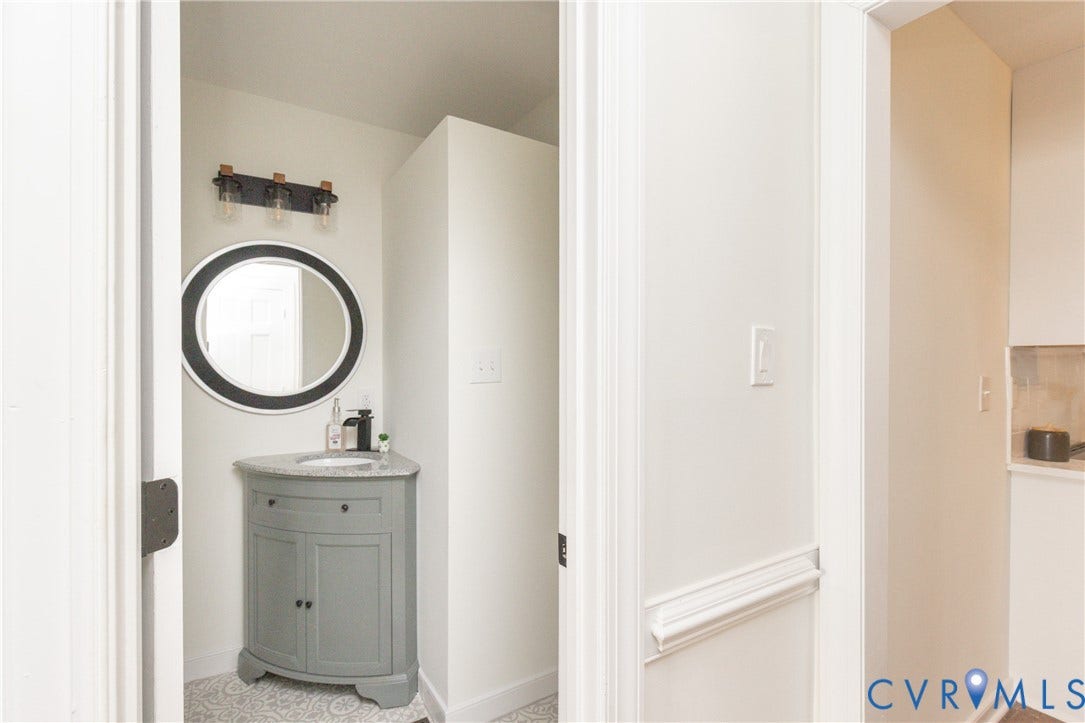 Corner vanity with granite-style countertop, circular mirror, and three-light fixture