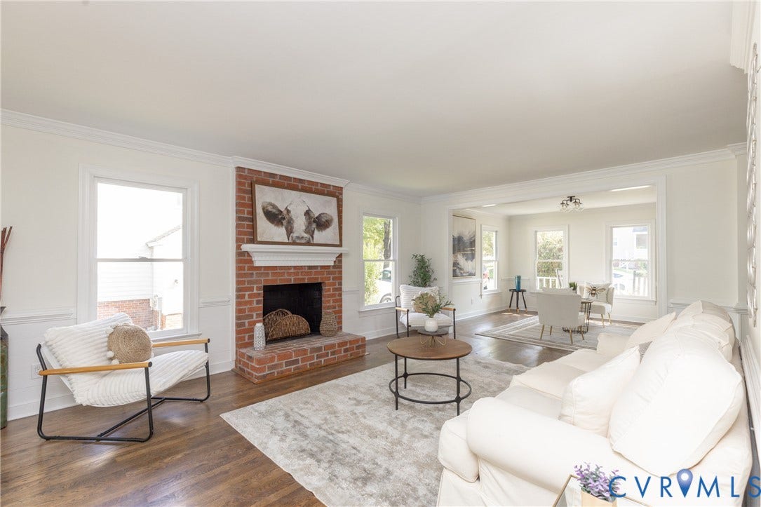 Brick fireplace with a white mantel, wood-finish flooring, white walls, and bright window light
