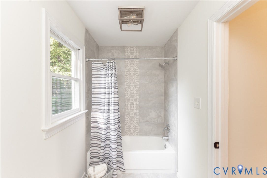 Bathtub with light gray tile surround, decorative tile accent, and polished chrome fixtures