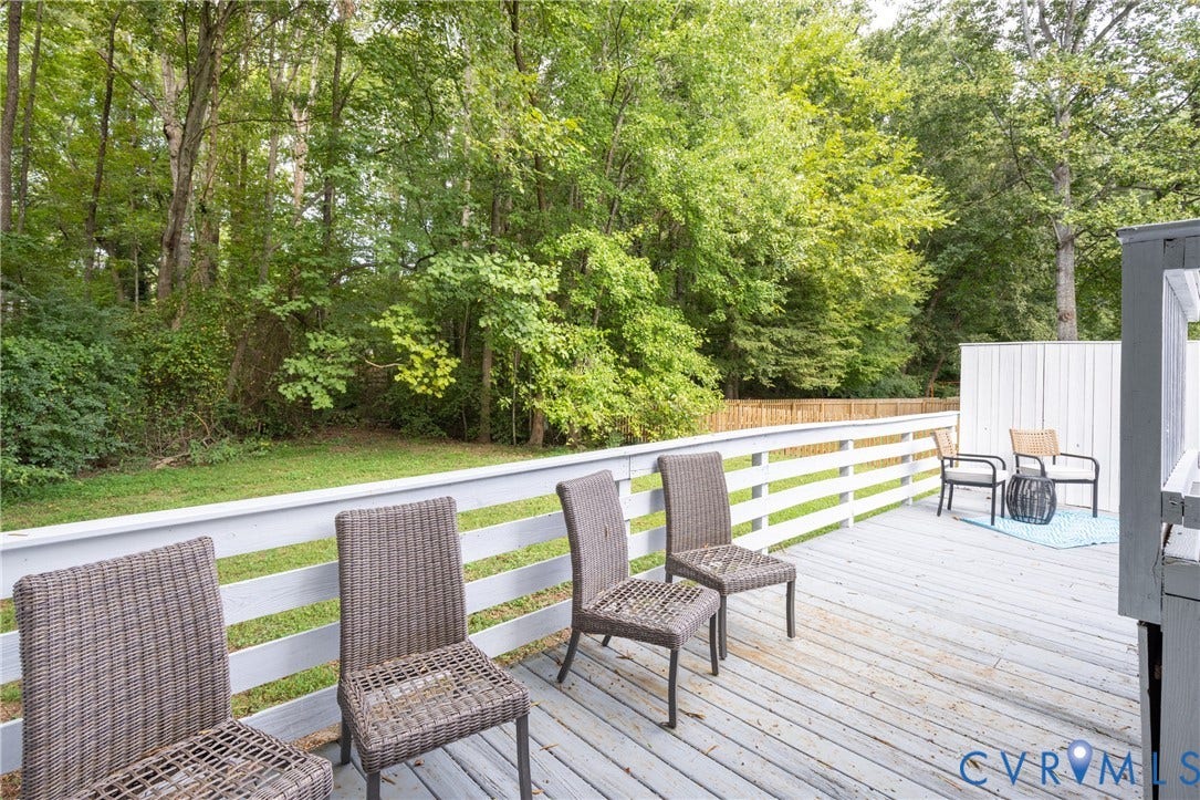 Expansive wood deck with painted railing, featuring a private fenced yard and mature trees