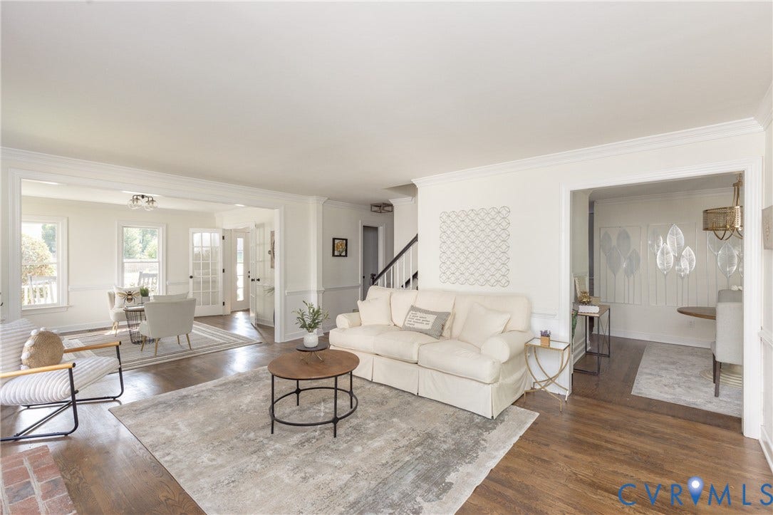 Open-concept living area with wood-finish flooring, white wall finishes, and extensive crown molding