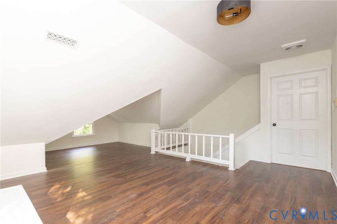 Expansive loft space featuring wood-finish flooring, white railing, recessed window, and overhead lighting fixture