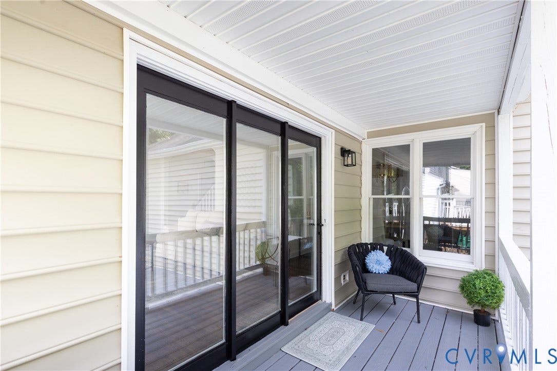 Sliding glass doors with dark framing, a light gray deck, a white railing, and an exterior wall light fixture