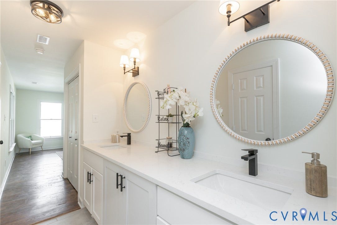 Dual vanity with integrated sinks, white cabinetry, matte black hardware and fixtures, and wall-mounted light fixtures