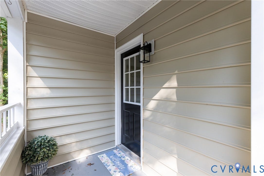 Porch entry with light-toned siding, black paneled door with glass inserts, and an exterior wall lantern