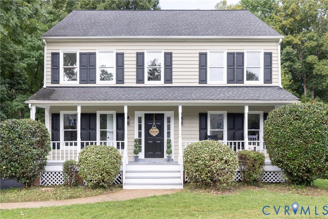 Two-story colonial-style residence with an inviting front porch, contrasting dark shutters, and a dark asphalt shingle roof
