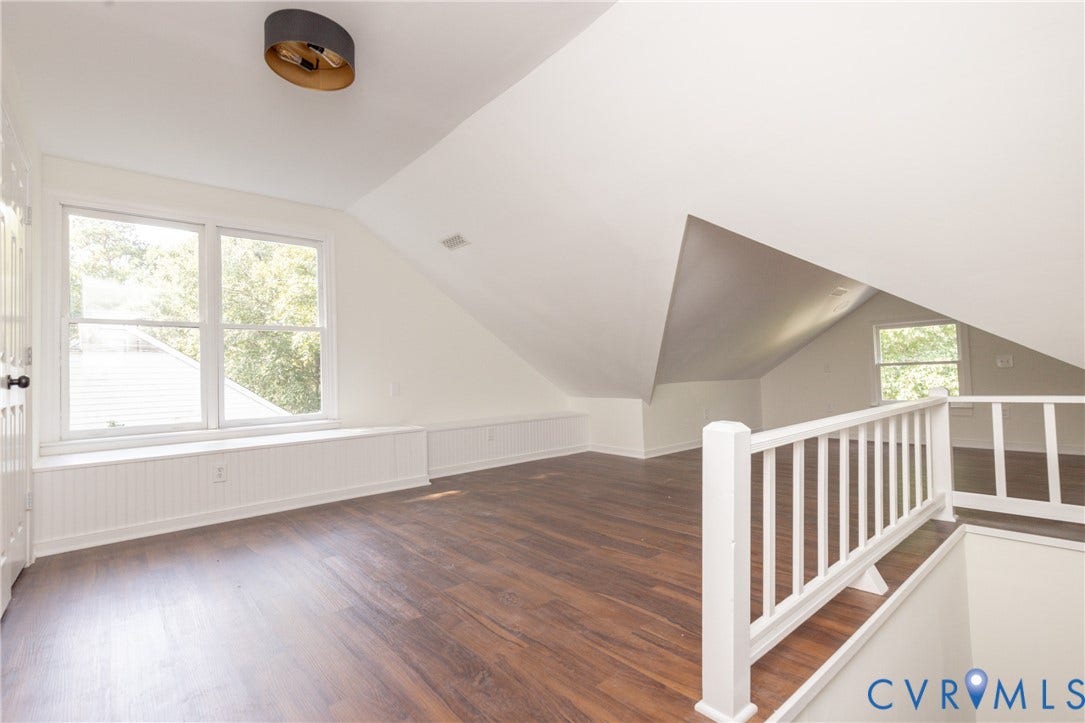 Expansive loft space featuring wood-finish flooring, multiple windows, a decorative railing, and a modern ceiling light fixture