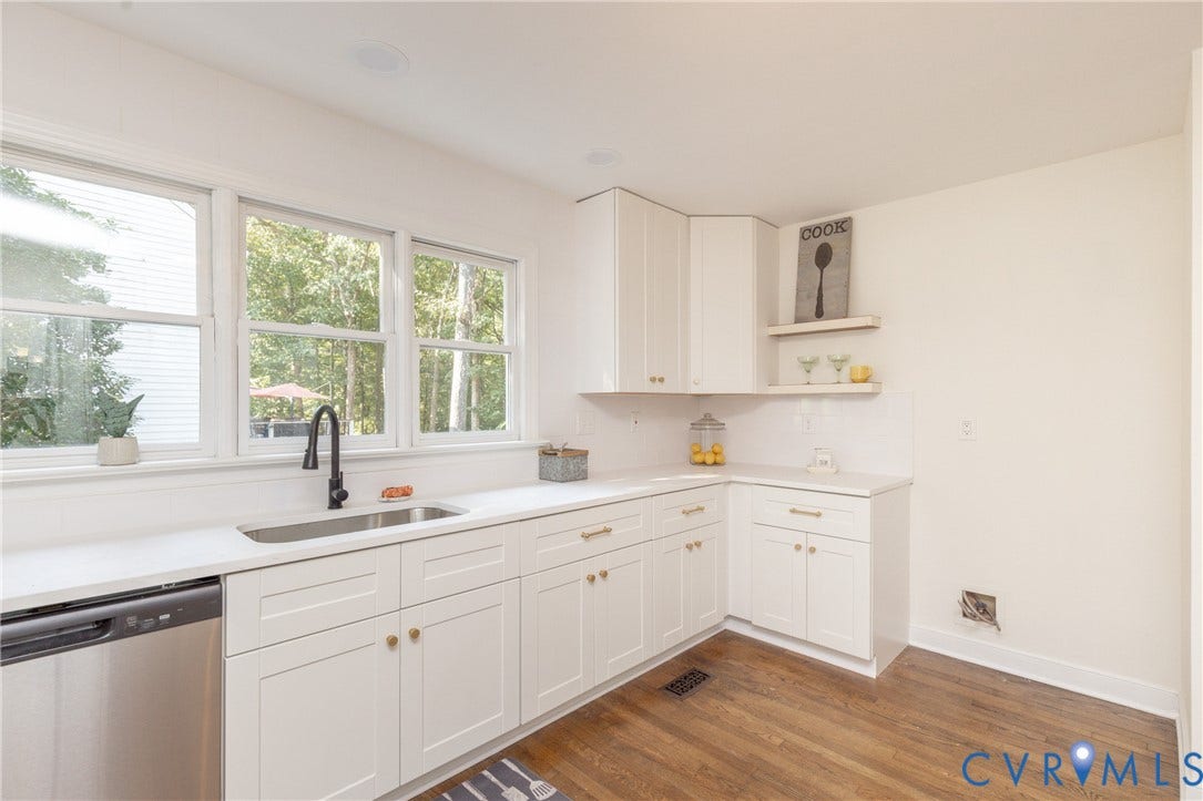 Kitchen featuring white cabinetry, wood-finish flooring, a stainless steel sink, and multiple windows providing natural illumination