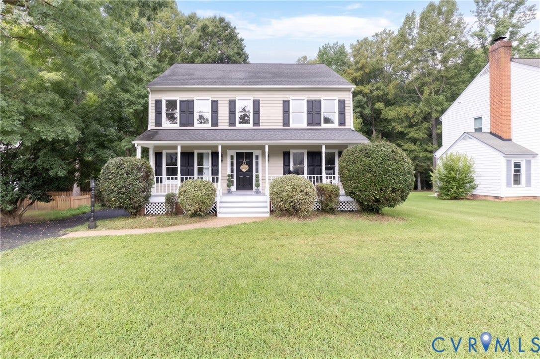 Traditional two-story residence featuring a covered front porch with white railings, a paved driveway, and established front landscaping