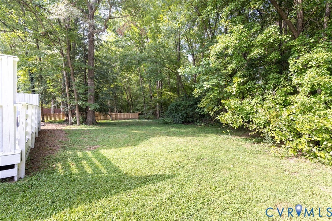 Expansive grassy yard with mature trees and a wooden privacy fence