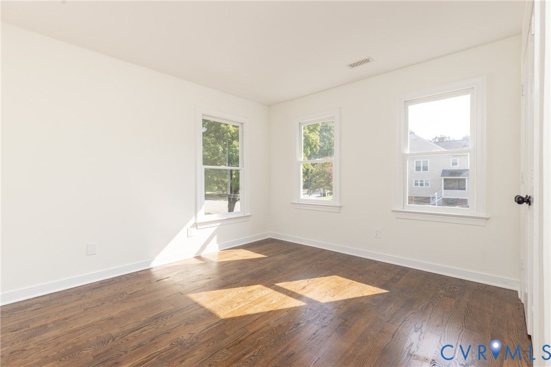 Wood-finish flooring, three windows with white trim, white walls, and a white door with a black knob