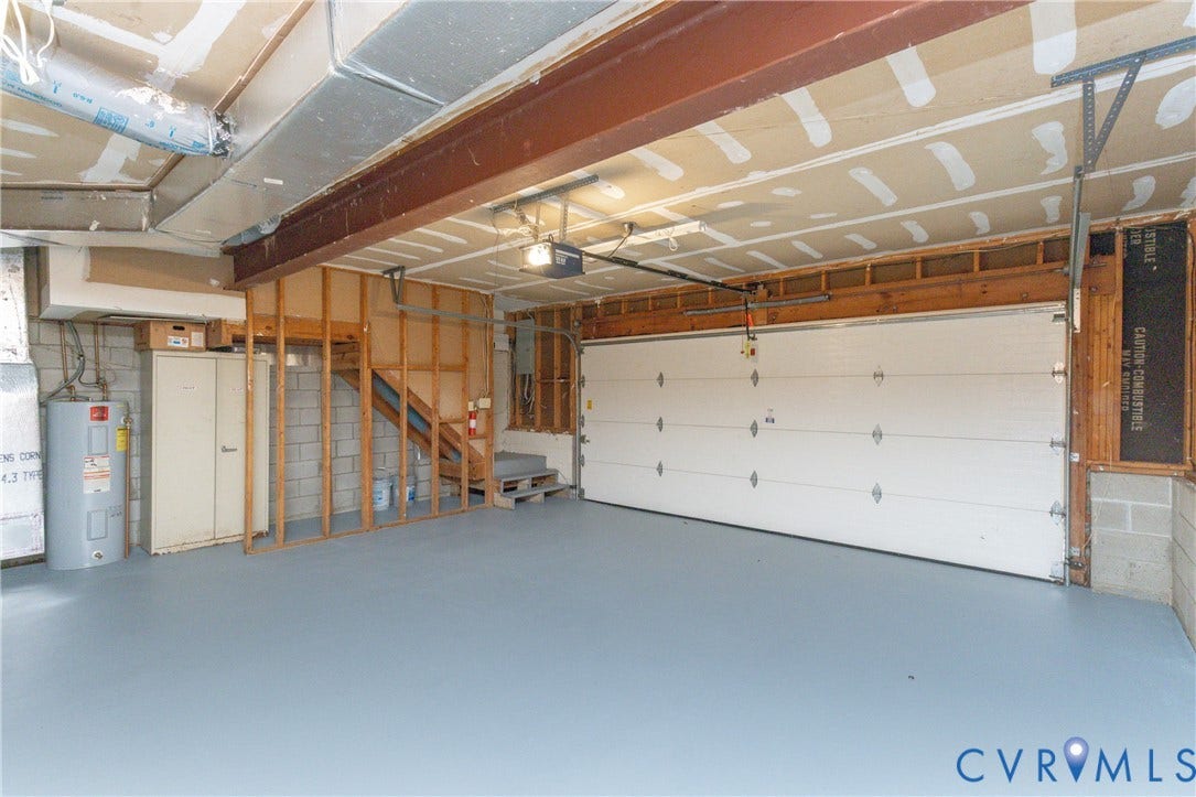 Expansive garage space featuring a roll-up garage door, concrete block wall, concrete flooring, exposed structural beams, and a water heater