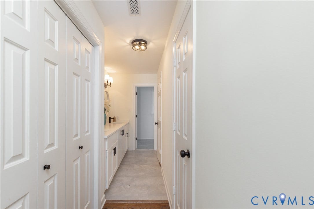 White panel doors, flush mount light fixture, vanity with white countertop, dark hardware on cabinetry, and wood-finish flooring