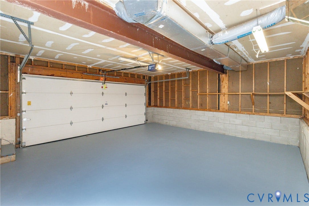 Spacious garage with a light gray floor, a large white garage door, and exposed structural elements