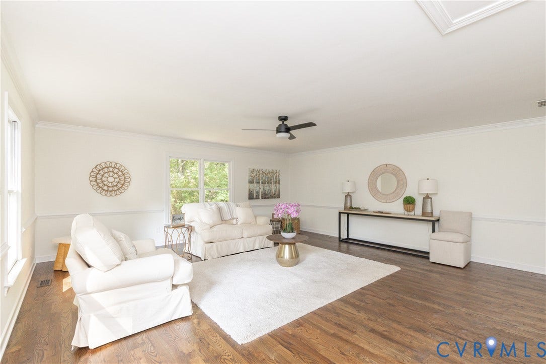 Spacious living area featuring wood-finish flooring, white walls with wainscoting, crown molding, and a ceiling fan