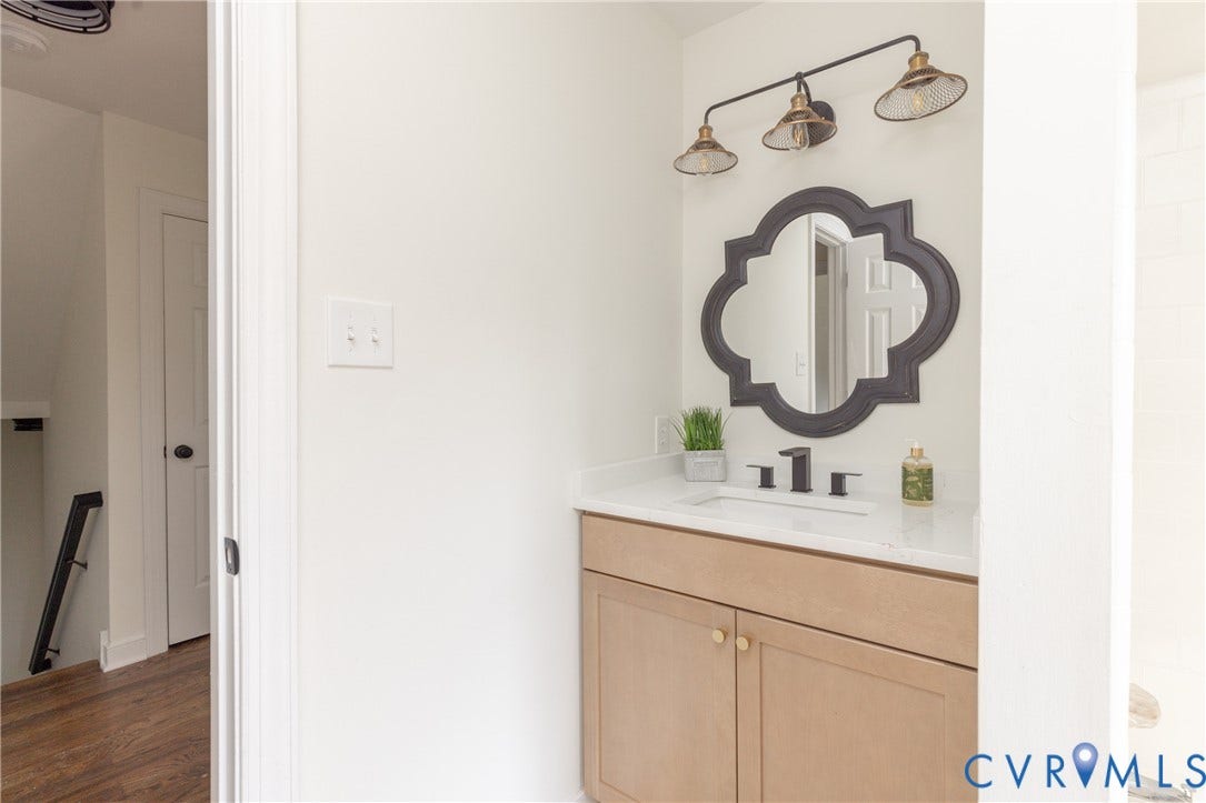 Vanity with a white countertop and integrated sink, matte black faucet, and light wood-finish cabinetry