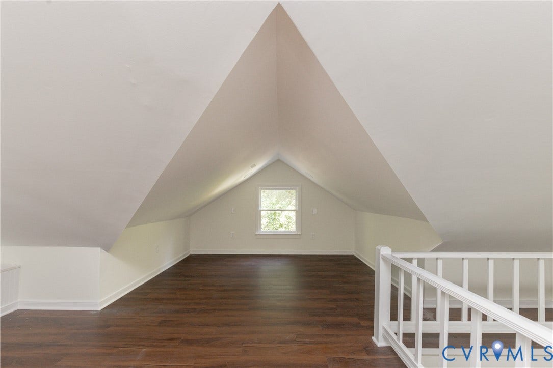 Sloped ceilings with recessed lighting, wood-finish flooring, white painted walls, and a window for natural illumination