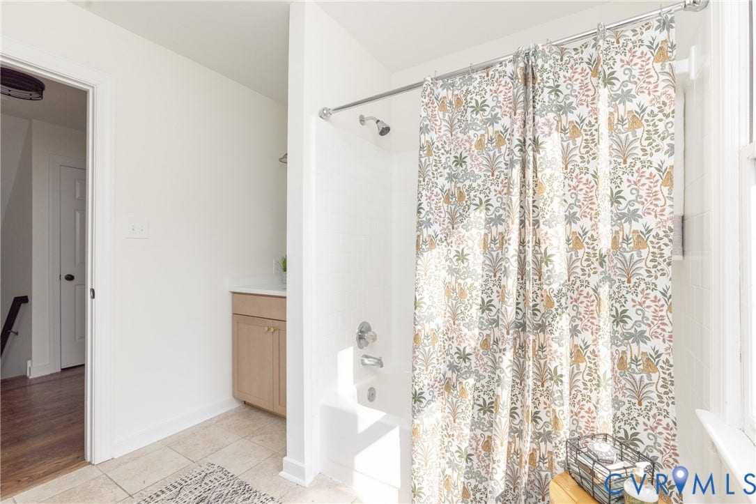 Bathtub with shower fixture, single vanity with wood-finish cabinetry, and tile flooring