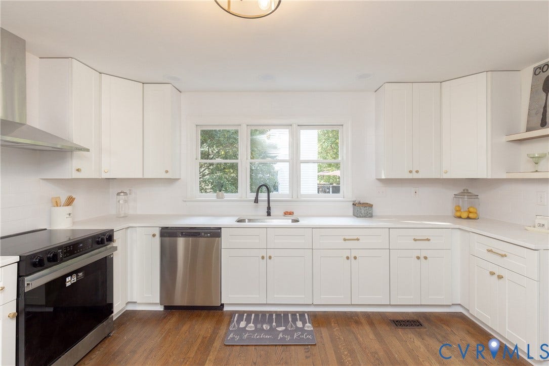 U-shaped kitchen with white cabinetry, wood-finish flooring, stainless steel appliances, and a window above the sink