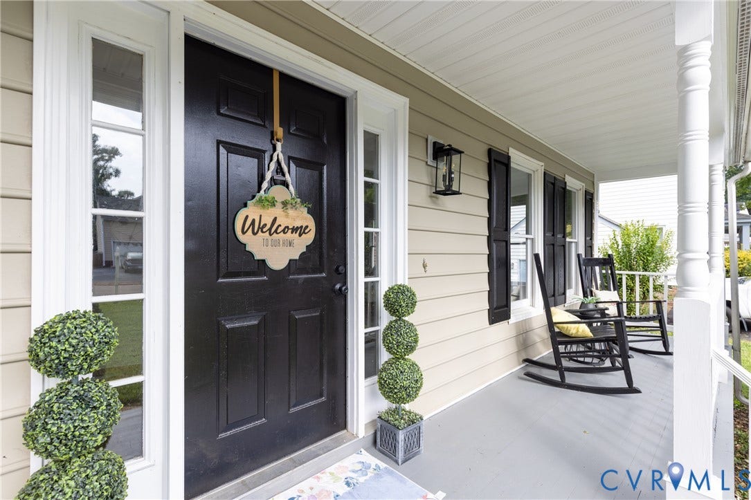 Covered front porch with white columns, black exterior shutters, exterior wall lantern, and light-colored siding