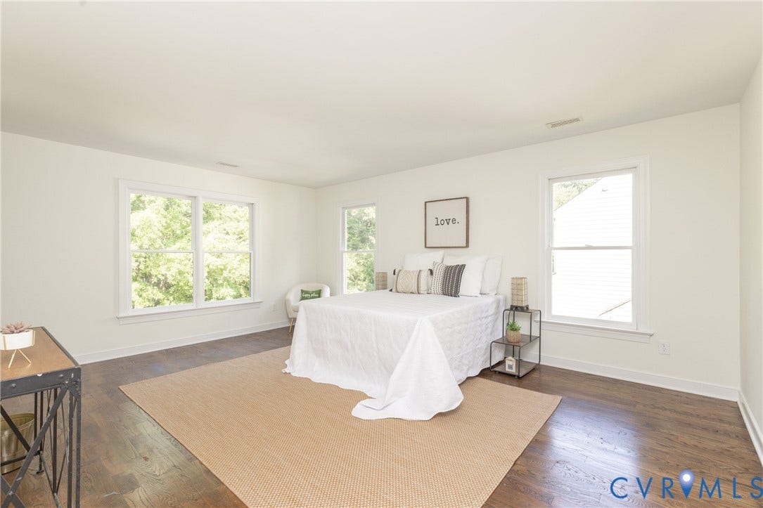 Spacious room with dark wood-finish flooring, white walls, and multiple windows