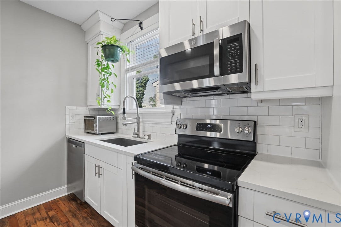 White shaker-style cabinetry, stainless steel appliances, undermount sink with gooseneck faucet, white subway tile backsplash, and light-toned countertops