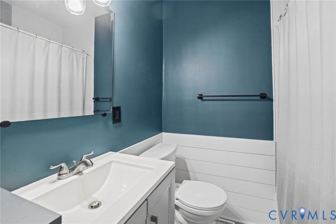 Bathroom featuring a vanity with an integrated sink, a rectangular mirror, a toilet, and shiplap wall detailing