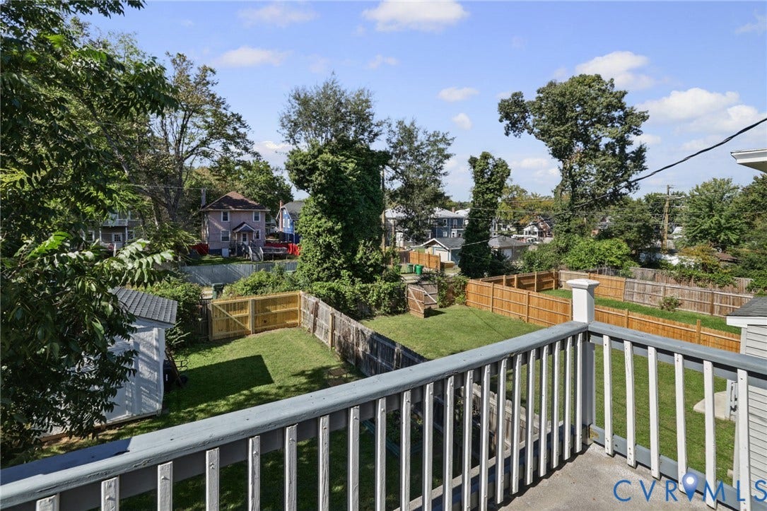 Expansive outdoor area featuring a wood fence, mature trees, a storage shed, and a concrete patio