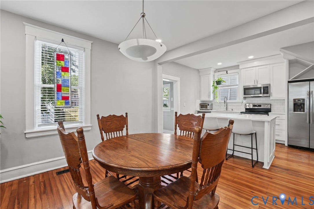 Wood-finish flooring throughout, white kitchen cabinetry, stainless steel appliances, kitchen island with seating, and a decorative pendant light fixture