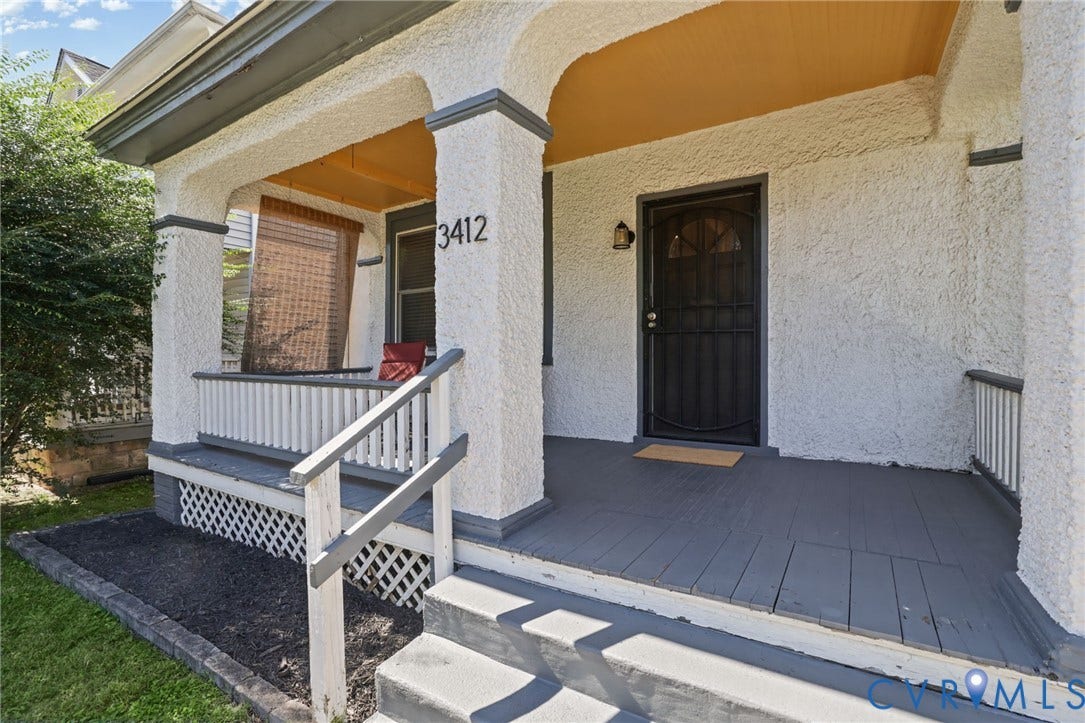 Front porch featuring wood flooring and railings, textured exterior walls, and an arched entryway